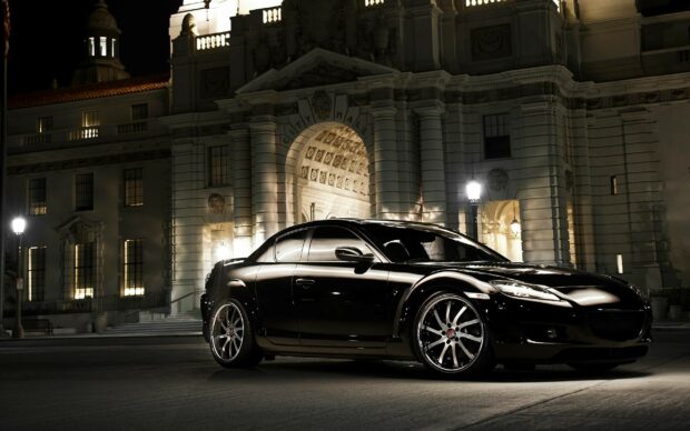A sleek black Mazda is parked in front of an illuminated historic city hall building at night, 2K Desktop Wallpaper