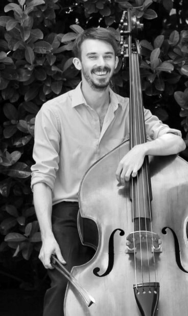 A smiling man is holding a double bass outdoors surrounded by leaves, HD Mobile Wallpaper