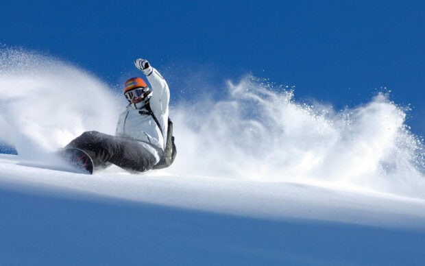 A snowboarder carving through fresh powder on a sunny snowy mountain slope
