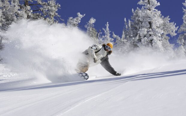 A snowboarder carving through fresh powder snow on a sunny mountain slope