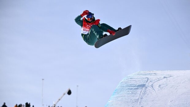 A snowboarder performing a jump over a snowy ramp in a snowboarding competition