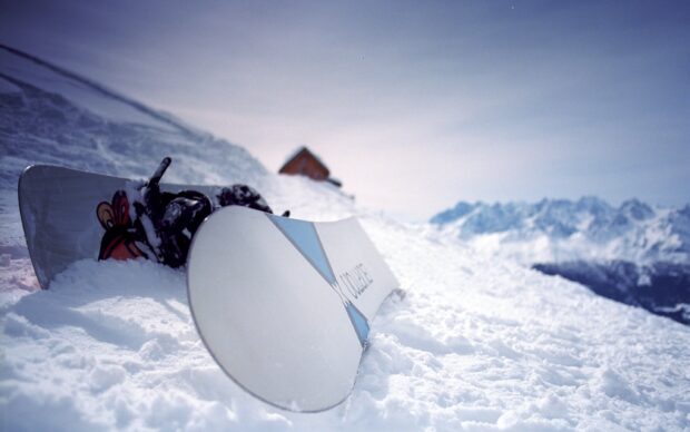 A snowboard placed on snow with mountain scenery in the background during a clear day