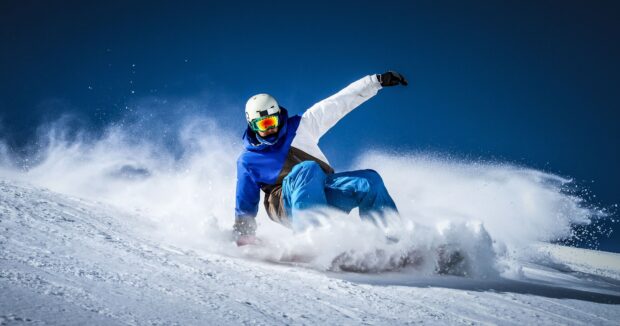 A snowboarder wearing a helmet and goggles sliding down a snowy slope in action