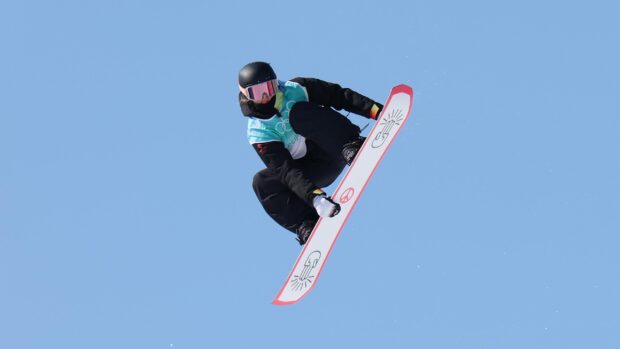 Snowboarding athlete performing a trick high in the air against a clear blue sky