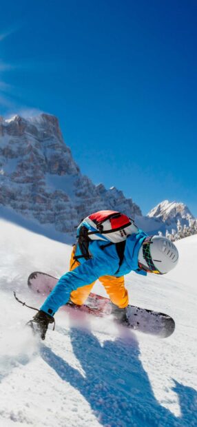 A snowboarder wearing bright clothing is snowboarding down a snowy mountain slope