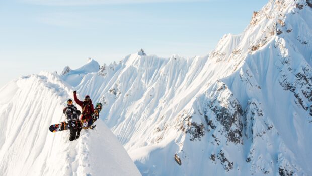 Two snowboarders standing on a snowy mountain ridge with snowboarding gear and snowboarding boards