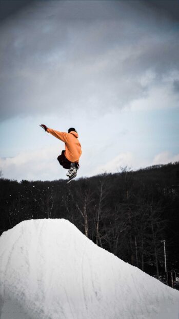 Snowboarder in orange jacket performing jump over snow ramp on winter day