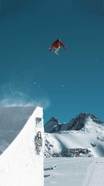 A snowboarder performing a trick in the air over a snow ramp in a snowy mountain area