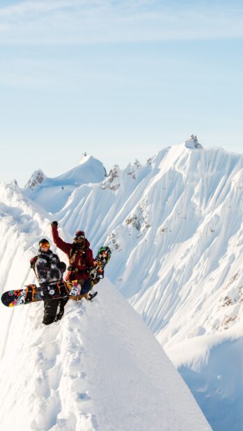 Two snowboarders standing on a snowy mountain ridge with snowboarding gear