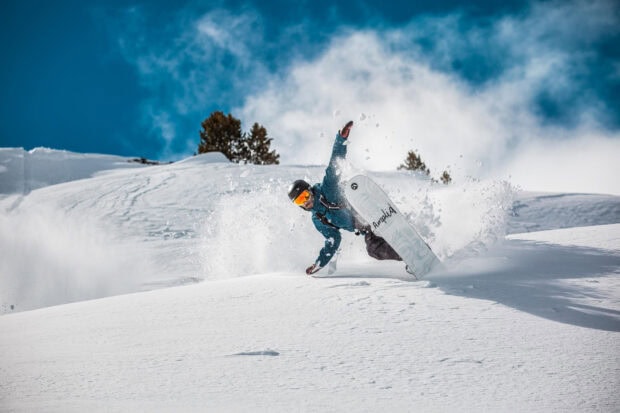 A snowboarder performing a dynamic snowboarding stunt on fresh snow powder with a clear blue sky background