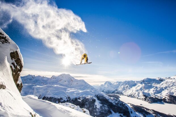 Snowboarding in the mountains performing a jump over fresh snow at sunrise