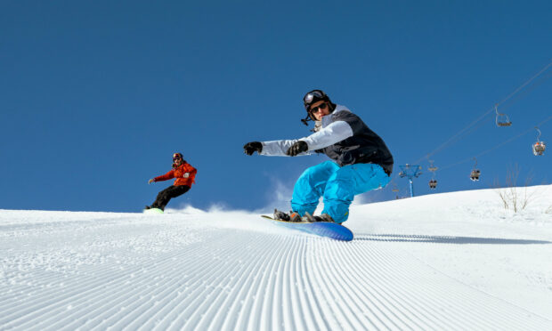 Two snowboarders wearing helmets and winter clothes snowboarding on a sunny groomed slope