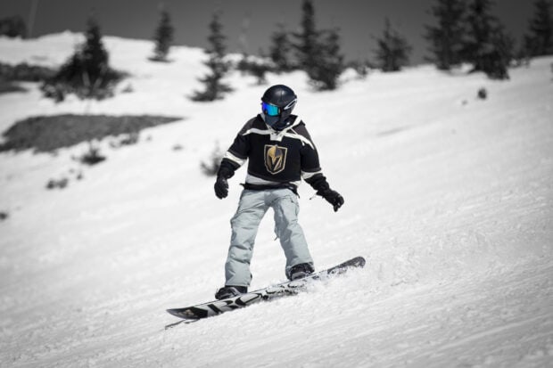 A snowboarder wearing a helmet and goggles gliding down a snowy slope