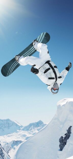 Snowboarding trick performed by a person wearing white snowboarding gear in snowy mountains