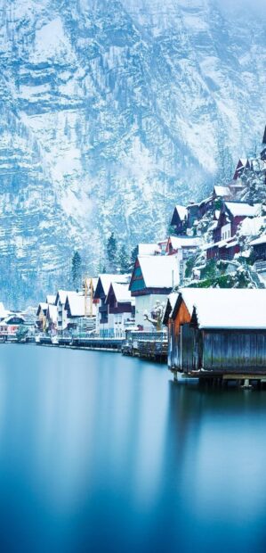 A snowy village with traditional houses reflects in the calm lake under towering mountains in Austria, HD Phone Wallpaper