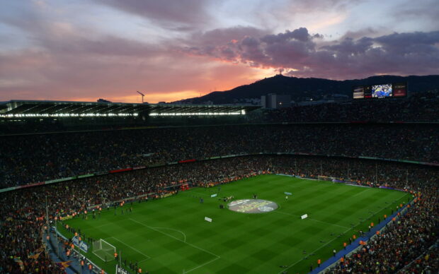 A large soccer stadium filled with fans under a colorful sunset sky