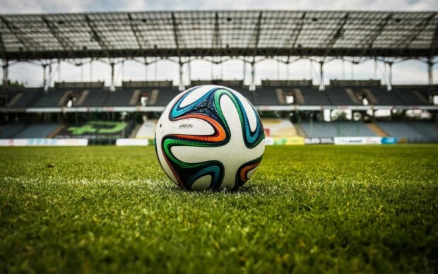 A soccer ball resting on the green grass of a stadium field with empty stands in the background