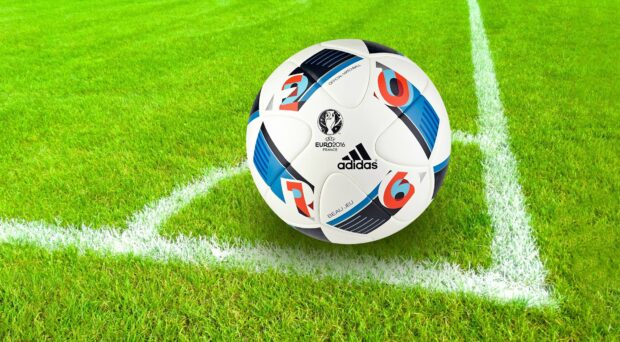 A classic soccer ball with UEFA Euro 2016 design on green grass near the corner line