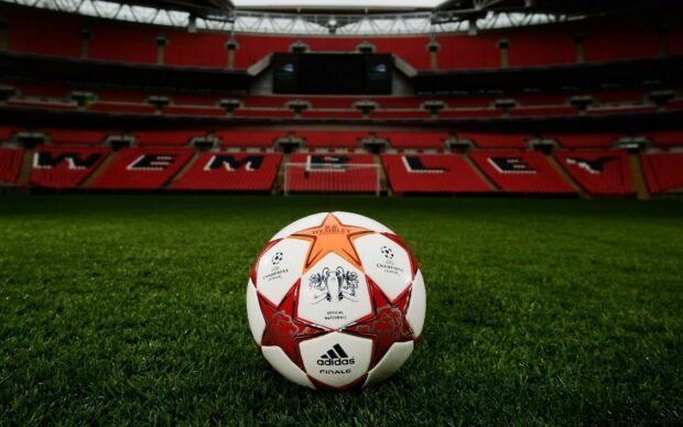 A classic soccer ball on grass in a large stadium with Wembley seats in the background