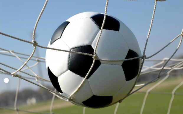 A soccer ball caught in the net during a sunny day on the field