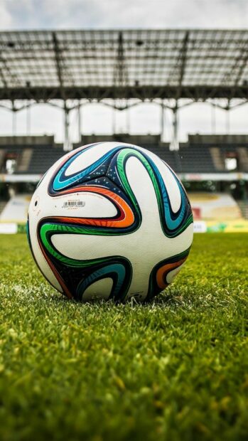 A colorful soccer ball placed on green grass inside a stadium on a soccer field