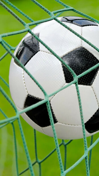 A soccer ball hitting the net during a game on a green field