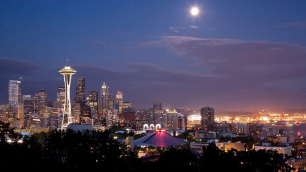 Evening city skyline featuring Space Needle structure under bright moonlight