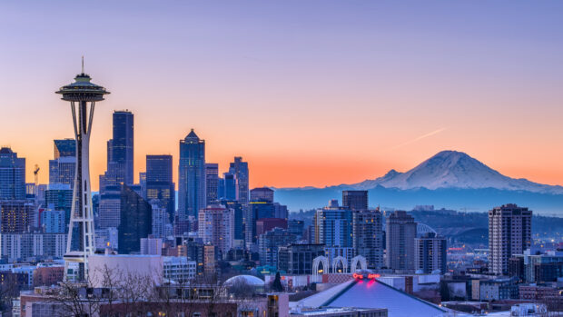 A panoramic view of the Space Needle and Seattle cityscape at sunset with Mount Rainier in the background