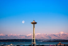 Space Needle structure with snowy mountains and full moon in clear sky