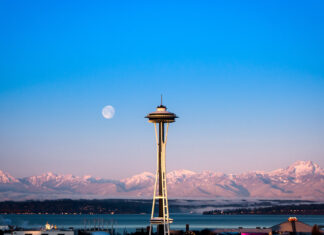 Space Needle structure with snowy mountains and full moon in clear sky