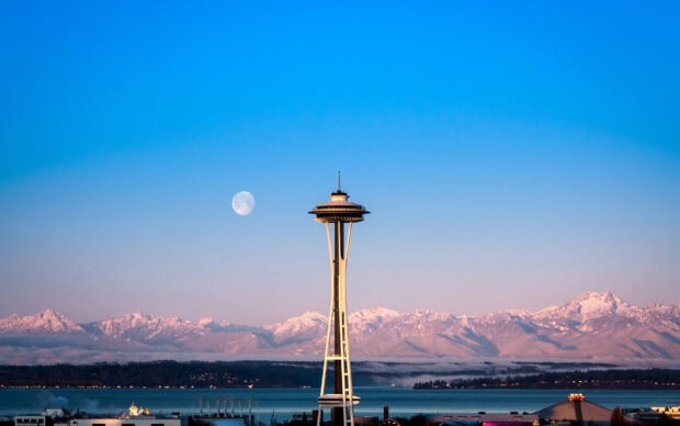Space Needle structure with snowy mountains and full moon in clear sky