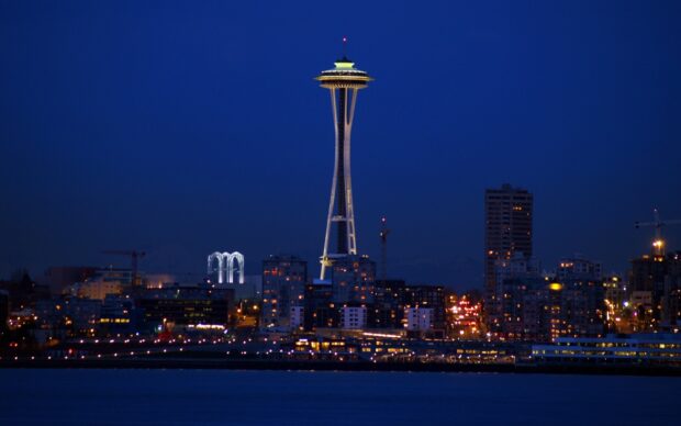Space Needle tower lit up over Seattle cityscape at night with clear dark blue sky