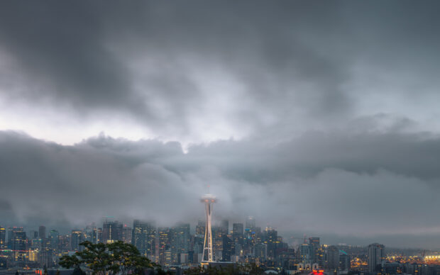 Space Needle tower rising above the Seattle skyline with low clouds and city lights visible