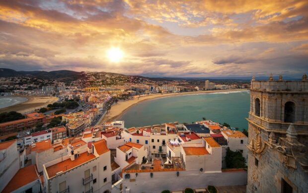 The Spain Wallpapers show a stunning coastal city with a beach and historic buildings at sunset, HD Desktop Wallpaper