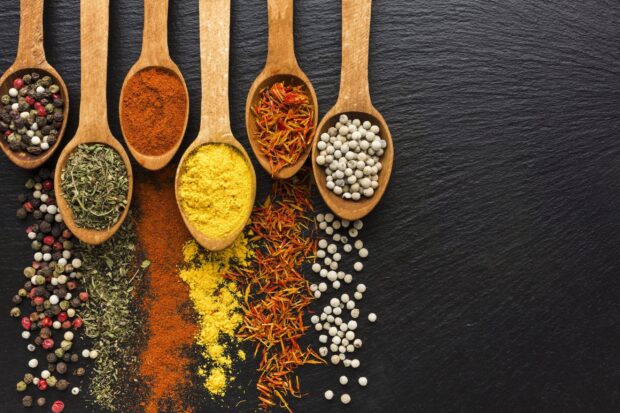 Various spices on wooden spoons with colorful herbs and powders arranged on a dark surface