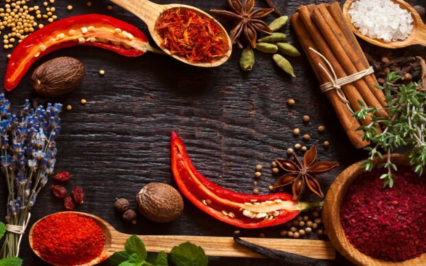 Various spices including chili peppers saffron and cinnamon sticks on a dark wooden surface