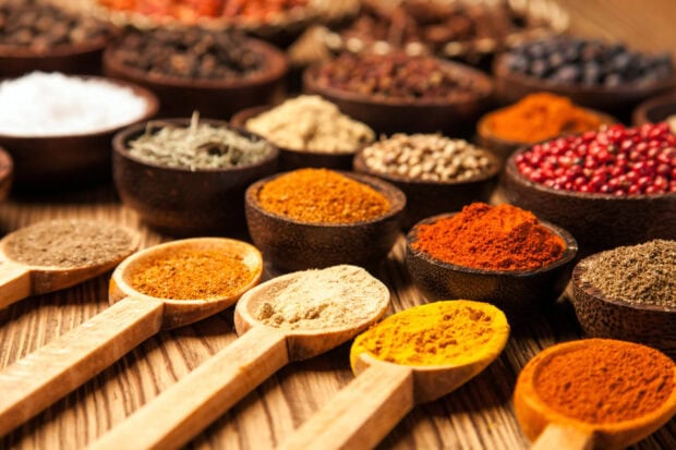 Various spices displayed in wooden spoons and bowls on a rustic wooden surface