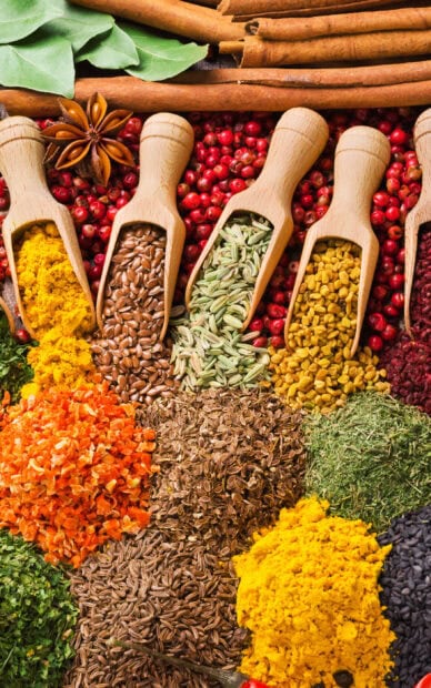 Assorted spices and seeds in wooden scoops with various dried herbs and powders displayed