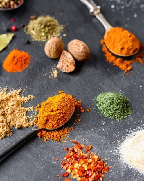 A variety of spices including nutmeg and dried herbs arranged on a dark surface