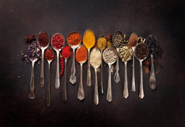A variety of colorful spices arranged on spoons on a dark surface