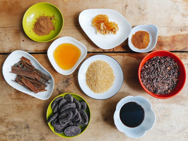 Various spices including cinnamon sticks and cocoa on a wooden table in a cooking setup
