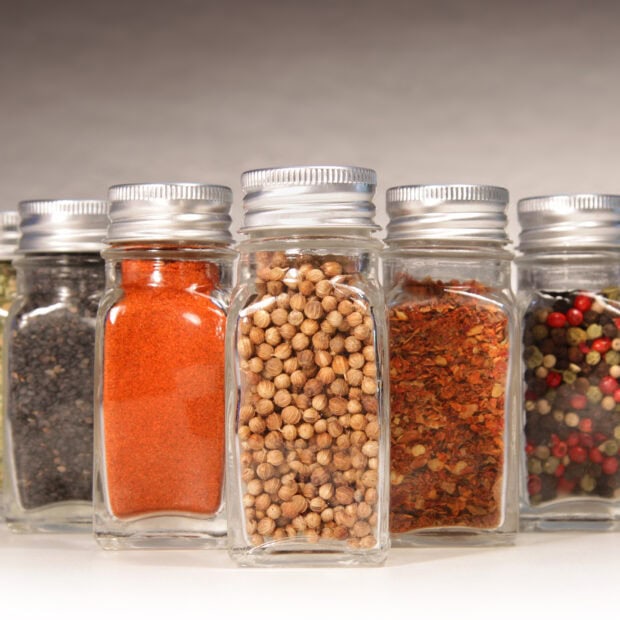 Glass jars filled with various spices including coriander displayed in a row
