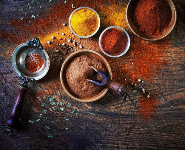Ground spices in bowls with wooden scoop on rustic table featuring spices