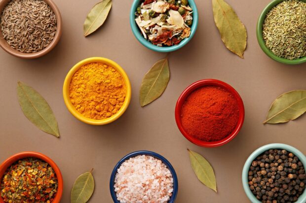 Various spices and dried herbs in bowls with bay leaves on a brown surface