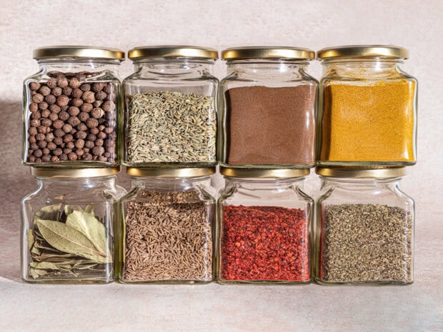 Various spices in glass jars arranged in two rows on a light surface