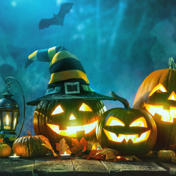A group of Halloween pumpkins glowing brightly with a lantern and autumn leaves on a wooden surface, HD Desktop Wallpaper