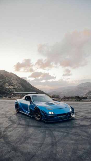 A blue Mazda is parked on asphalt with mountains and clouds in the background showing Mazda Wallpapers, HD Phone Wallpaper
