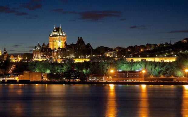 A nighttime view of St Lawrence River with illuminated historic buildings and calm water reflections