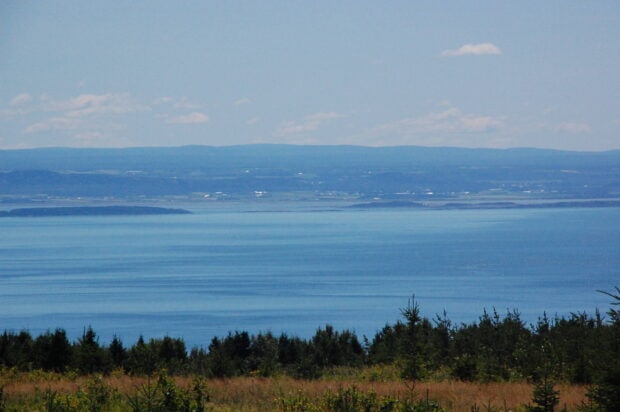 A clear blue view of the St Lawrence River with hills and trees under a partly cloudy sky