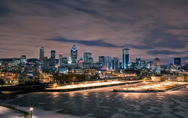 Night view of the St Lawrence River with a city skyline illuminated by lights under cloudy skies